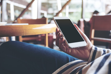 Mockup image of hands holding white mobile phone with blank black screen in wooden cafe
