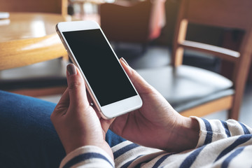 Mockup image of hands holding white mobile phone with blank black screen in wooden cafe