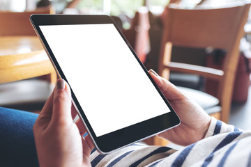 Mockup image of woman's hands holding black tablet pc with blank white desktop screen while sitting in cafe