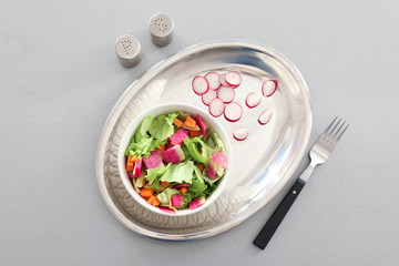 Fresh salad with sliced radish and lettuce in bowl on light background