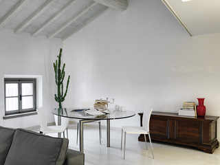 interior shot of a modern living room in the attic room in the foreground the glass dining table with white chairs and old trunk