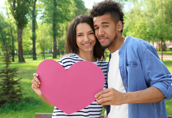 Happy African-American couple with paper heart in park on spring day