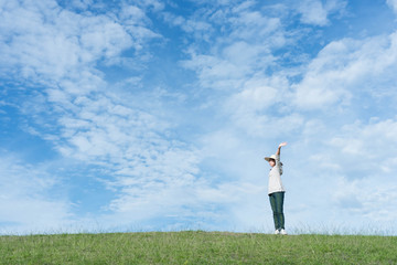 Standing woman raised her hands on the mountain, natural green and beautiful sky.