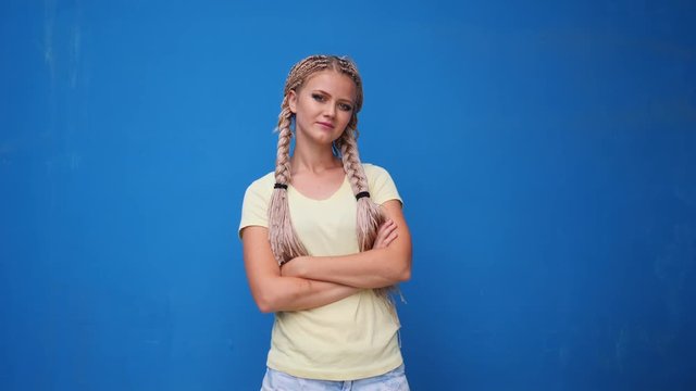 Serious blond hipster student woman looking at camera with arms crossed over blue background