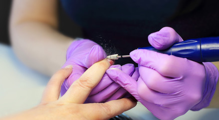 Manicure salon. The master does a manicure to a young woman. Gloves on the hands of the master. The concept of beauty. Selective focus, copy space, close-up.