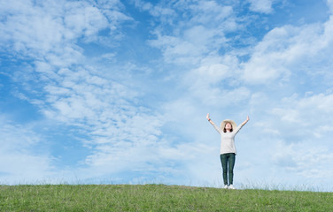 Standing woman raised her hands on the mountain, natural green and beautiful sky.