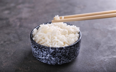 Chopsticks and bowl with boiled white rice on grey background