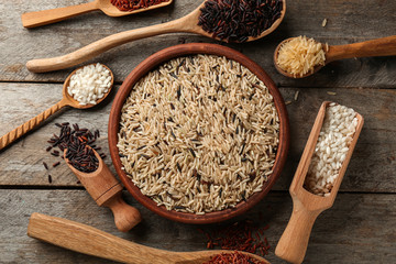 Different types of rice in kitchenware on wooden table