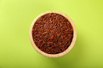 Wooden bowl with raw red rice on color background