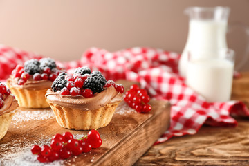 Wooden board with tasty tartlets on table