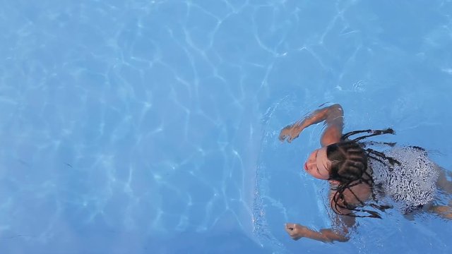 Dark-haired slim girl having a swim in the pool, enjoying clean blue water in morning time while being on holidays
