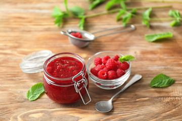 Bowl of tasty jam and glass jar with raspberry on wooden table
