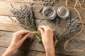 Woman tying bunch of beautiful lavender flowers on wooden table