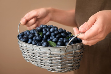 Woman holding basket with ripe blueberries on color background