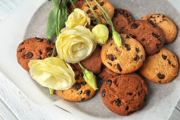 Plate with tasty chocolate cookies and flowers on wooden table