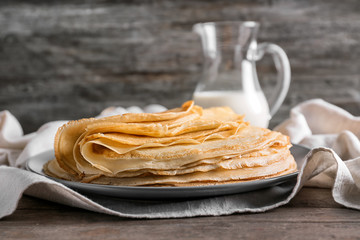 Plate with stack of tasty thin pancakes on wooden table