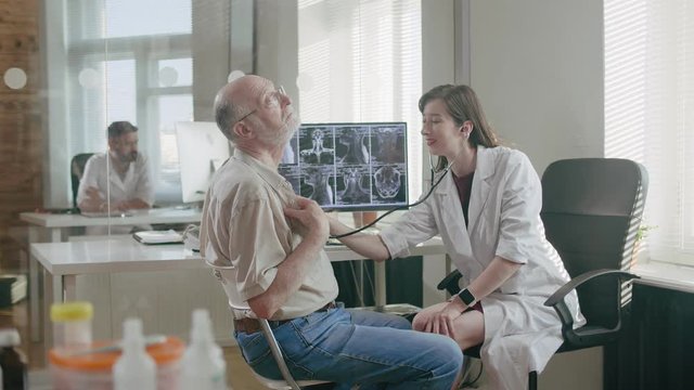 Girl nurse listens breathing and heartbeat of elderly patient using stethoscope. Therapeutic department of medical center. Grandfather visit to doctor