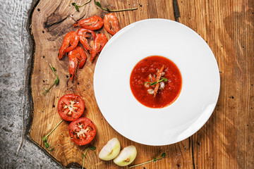 Tasty tomato soup with shrimps in plate on wooden table