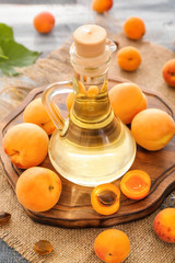 Glass jug with essential oil and fresh apricots on table