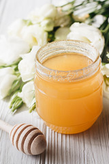 Honey dipper, honey and white flowers on wooden board