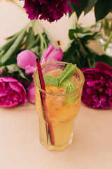 Delicious tropical cocktail with mint leaves, pink peony flowers on table