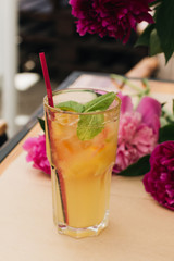 Delicious tropical cocktail with mint leaves, pink peony flowers on table