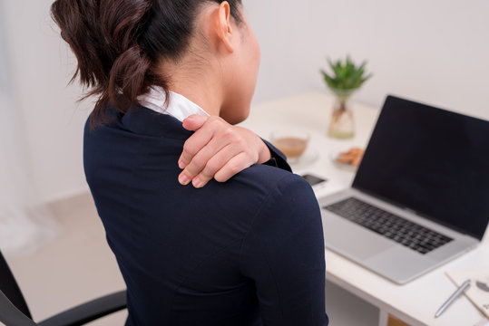 Young business person with neck pain. Focus on hand on neck with laptop on table in background.