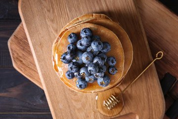 Board with tasty pancakes, honey dipper and blueberries on wooden table