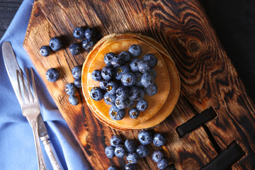 Board with tasty pancakes and blueberries on table