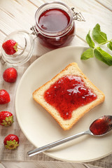 Plate with slice of bread and delicious strawberry jam on white wooden table