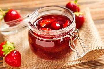 Glass jar with delicious strawberry jam on wooden table, closeup