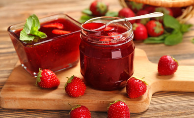 Glass jar and bowl with delicious strawberry jam on wooden table