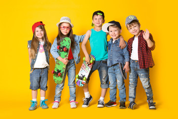 Group fashion cute preschooler kids friends together with skateboards is looking at camera on a yellow background. friendship, fashion, summer concept. Space for text.