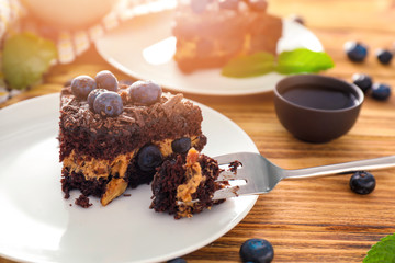 Plate with piece of blueberry chocolate cake on wooden table, closeup