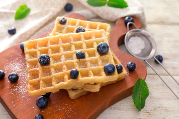 Board with delicious waffles and blueberries on wooden table