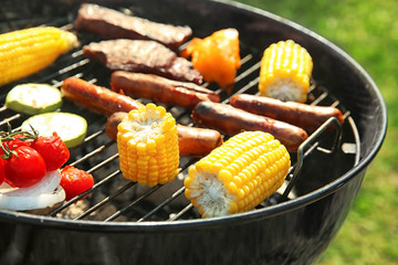 Tasty meat with vegetables and sausages being cooked on barbecue grill outdoors, closeup