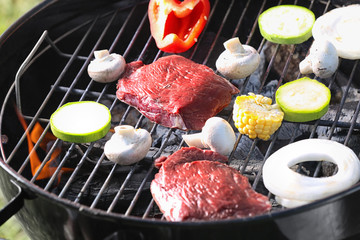 Tasty steaks and vegetables cooking on barbecue grill, closeup