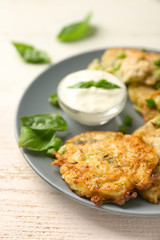 Plate with zucchini pancakes and sauce on wooden table