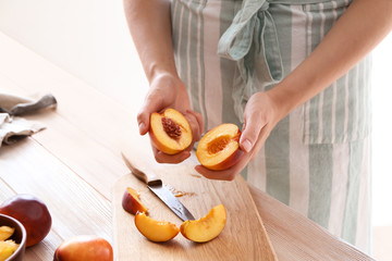 Obraz na płótnie Canvas Woman holding halves of sweet peach at wooden table