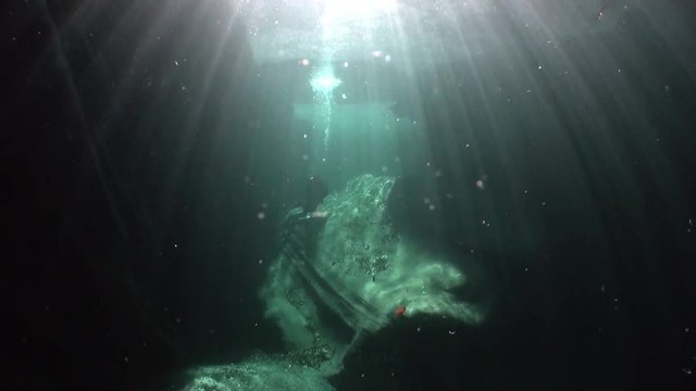 Camera operator in refraction of sunlight underwater in river Verzasca. Shooting a frame of picturesque nature on background of huge smooth stones.