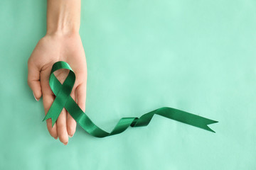Woman holding green ribbon on color background. Kidneys cancer awareness concept