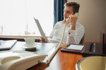 Portrait of handsome young entrepreneur speaking by phone and using laptop while working in...