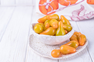 Ceramic bowl with yellow pear tomatoes on white wooden background. Free space