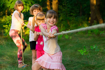 Group of happy children playing tug of war outside on grass. Kids pulling rope at park. Summer camp fun