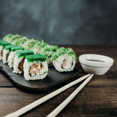 Japanese restaurant, sushi plate. Delicious seafood maki rolls on black wooden tray with sauce and chopsticks