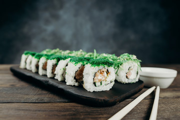 Japanese restaurant, sushi plate. Delicious seafood maki rolls on black wooden tray with sauce and chopsticks, copy space
