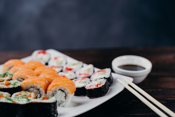 Japanese restaurant, sushi plate. Appetizing seafood maki rolls set on white plate with sauce and chopsticks, copy space