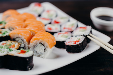 Japanese restaurant, traditional seafood, sushi plate. Delicious  maki rolls set on white plate with sauce and chopsticks, selective focus