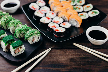 Japanese restaurant, sushi plate. Delicious seafood maki rolls on black plates with sauce and chopsticks