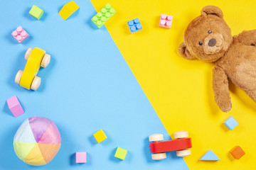 Baby kids toys frame with teddy bear, wooden toy car, colorful bricks on blue and yellow background. Top view